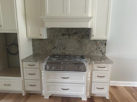 White kitchen cabinets surround a stovetop with a granite backsplash.
