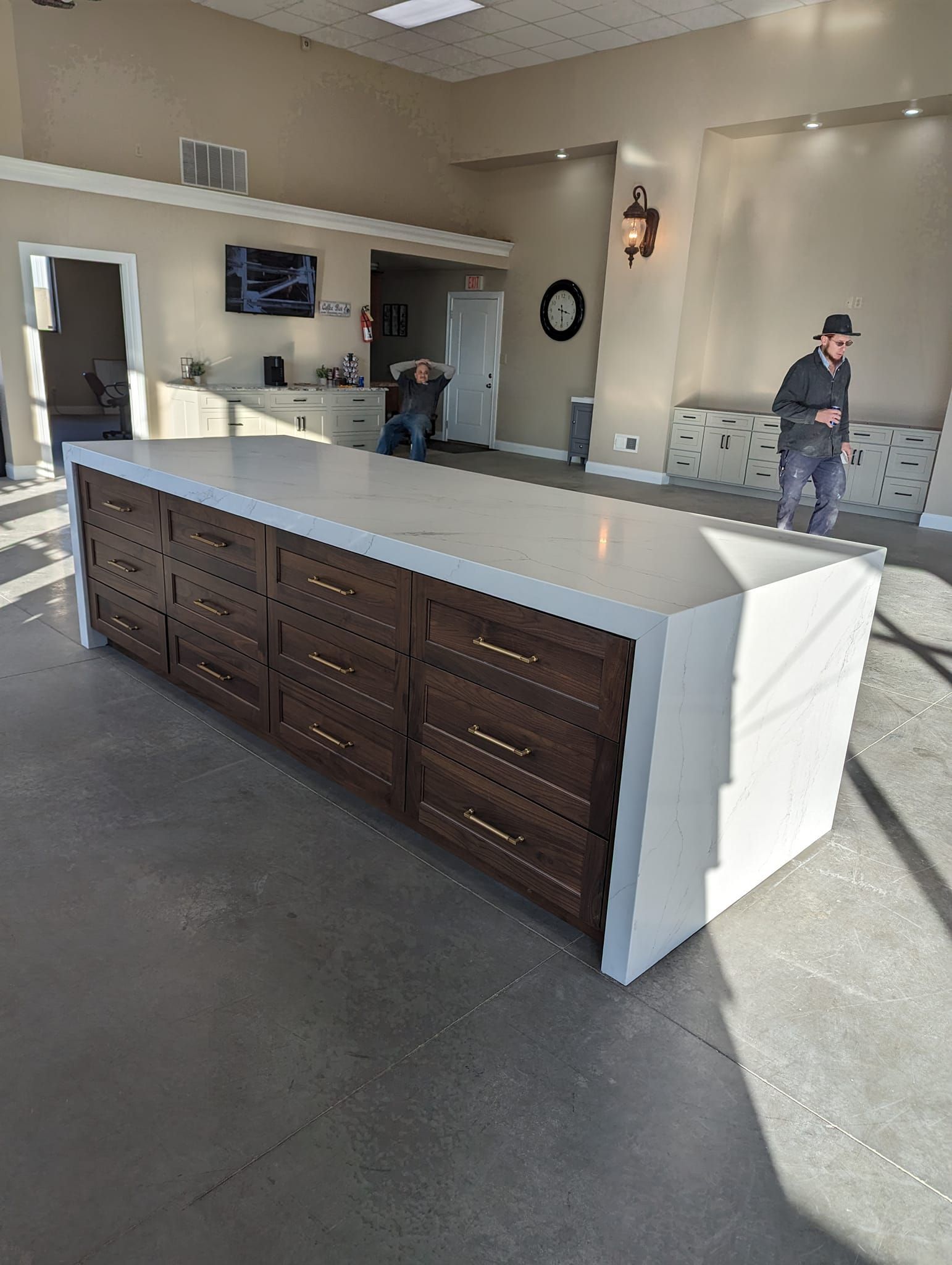 Large kitchen island with dark wood cabinets, light countertop, and gold hardware. Man standing near a cabinet.