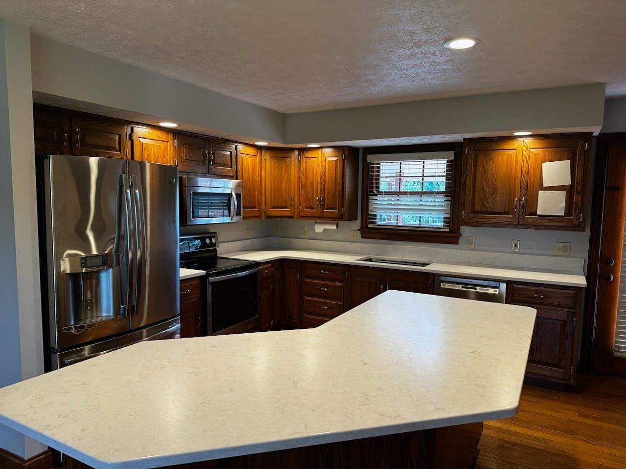 L-shaped kitchen with wooden cabinets, stainless steel appliances, and a white countertop island.