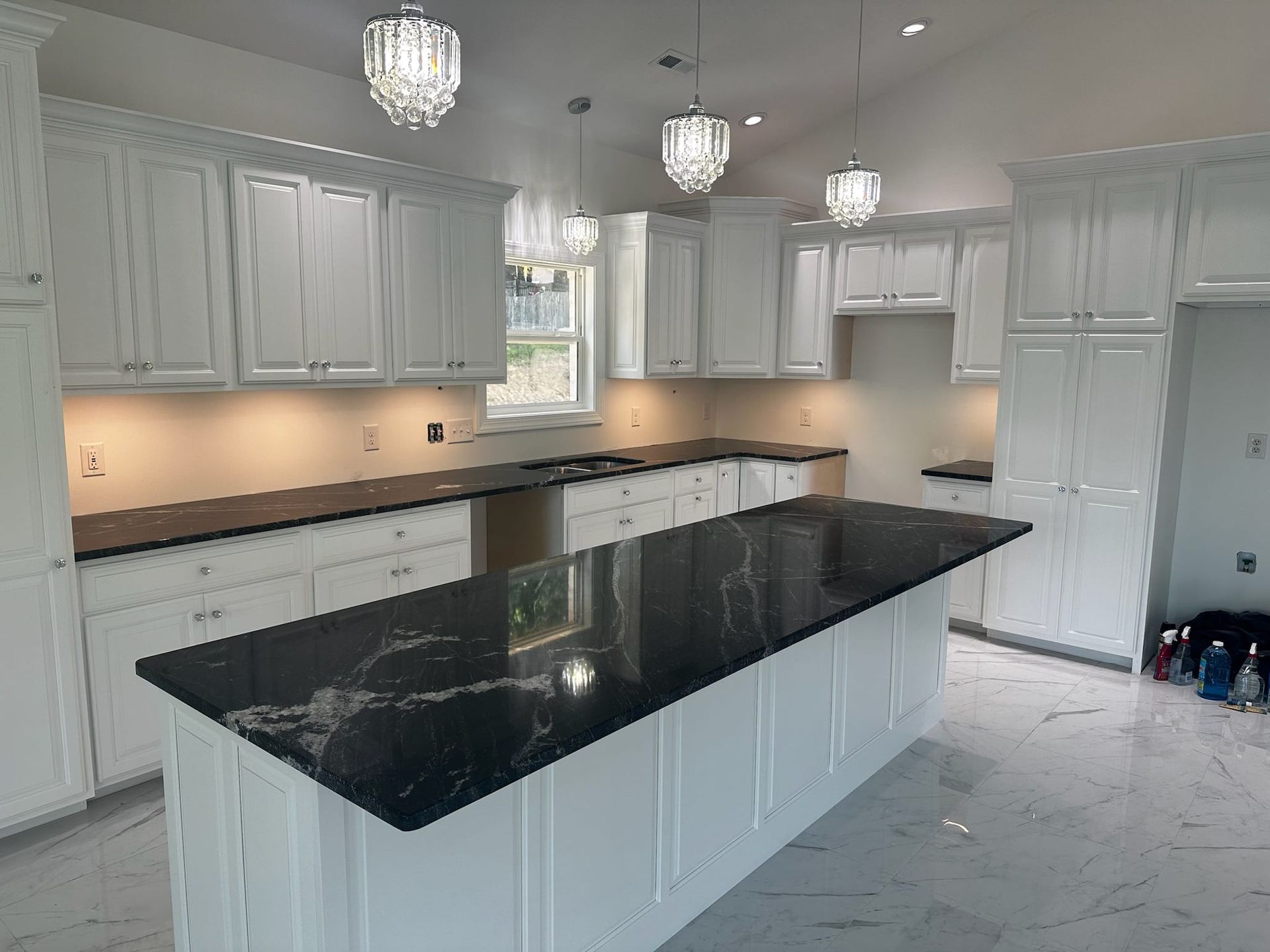White kitchen with dark countertops and island, pendant lights, and white cabinetry.