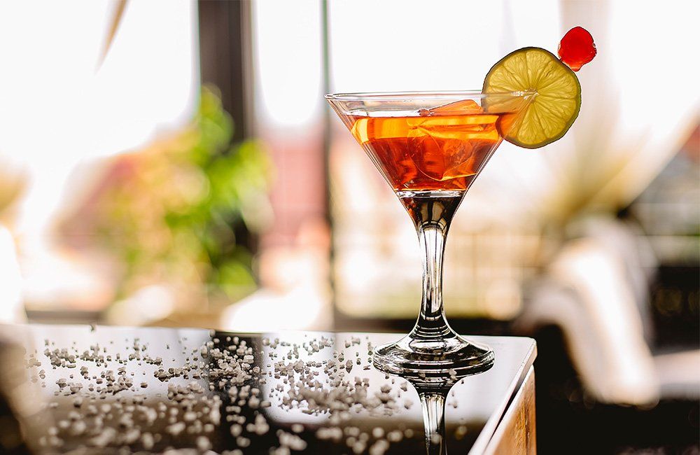 A martini glass with a cherry and lime on a bar.