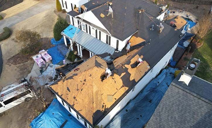 Workers repairing a roof with some sections missing, surrounded by tarps and supplies.
