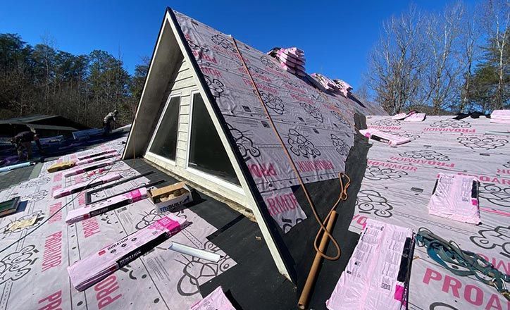 Roof of a building during construction; pink insulation, window, blue sky, and someone working.