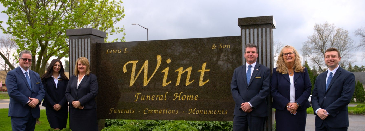 People in suits posing beside a “Wint” entrance sign at a gated residential community