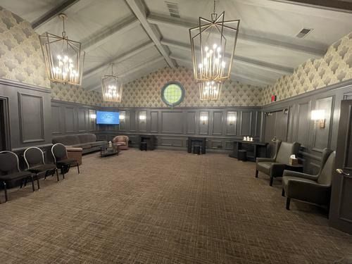 Empty meeting room with gray paneled walls, chandeliers, chairs, and a TV screen on the left.