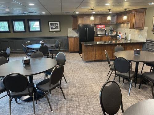 Empty cafeteria seating area with round tables, black chairs, and a kitchenette counter in the background