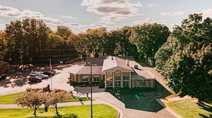 Aerial view of a small brick building with a parking lot, surrounded by trees and green lawn.