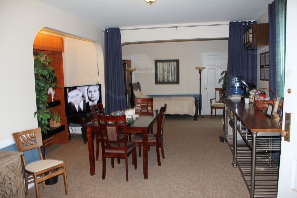 Spacious living area with a dining table, TV, and kitchen counter. Blue curtains divide the room.