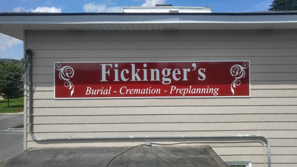 Sign for Fickinger's, a funeral home, on a beige building. The sign is red with white text, offering burial, cremation, and preplanning services.