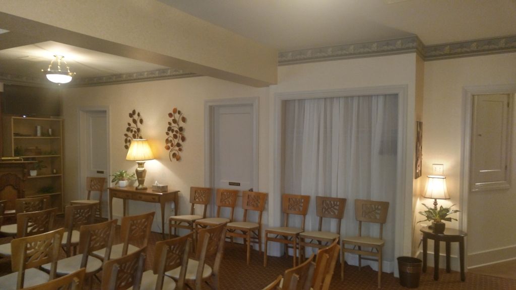 An interior shot of a room with chairs arranged for a gathering. Light beige walls, a decorative border, and two lamps illuminate the space.