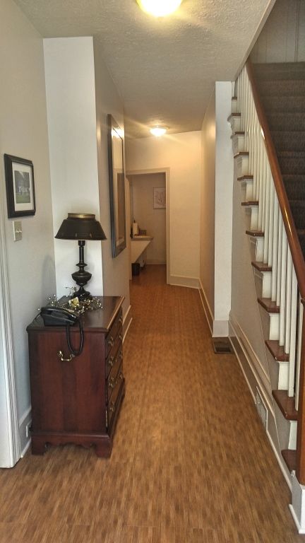 Hallway with wooden floors, stairs on the right, and a dark wooden cabinet with a lamp. A bathroom is at the end.