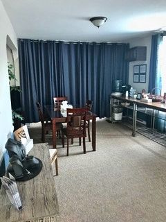 A dining room with a dark blue curtain separating the dining area from the kitchen. A wooden table and chairs are in the center.