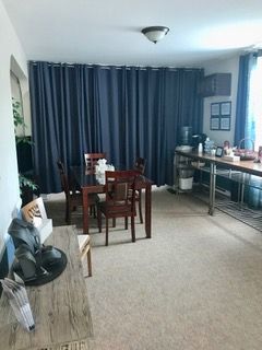 A dining room with a dark blue curtain wall. A table and chairs are set, with a kitchen counter and storage in the background.