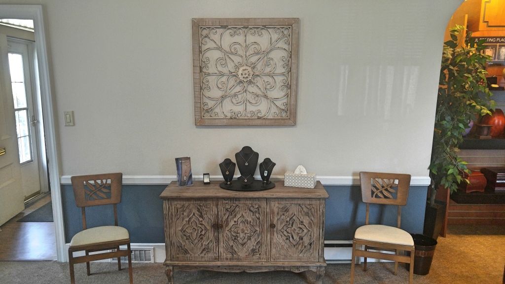 Entryway with a light blue and white wall, a wooden cabinet with jewelry, chairs on either side, and decorative wall art.