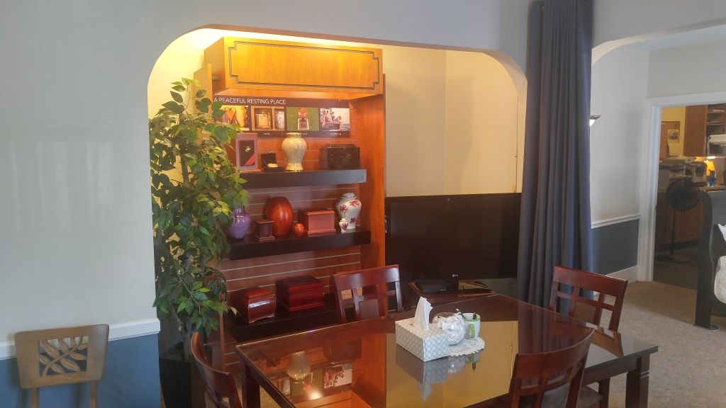 Dining room with a dark wood table, chairs, and a built-in bookshelf with decor. A large plant is to the left.