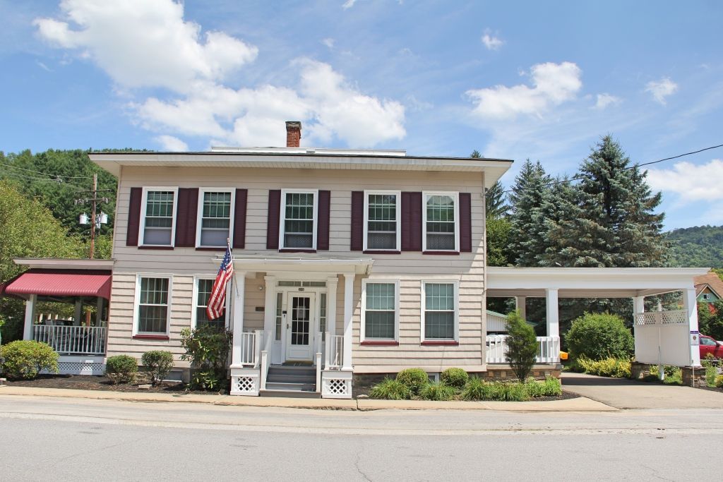 Gray building with a covered entrance, double doors, and windows. Two green bushes flank the entrance.