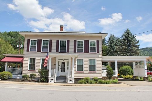 Gray building with a covered entrance, double doors, and windows. Two green bushes flank the entrance.