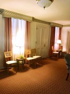 A waiting room with red carpet, chairs, curtains, a lamp, and a door.