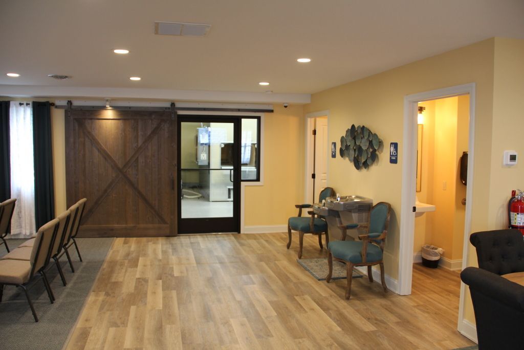 Interior room with light wood flooring, beige walls, and a large wooden barn door. Chairs are set up in the left foreground.