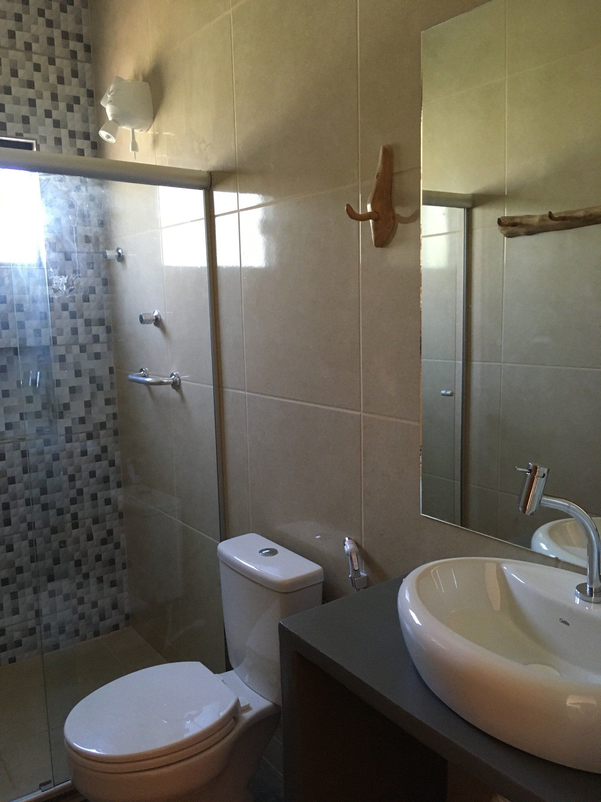Banheiro com vaso sanitário, pia, chuveiro com mosaicos e espelho grande.