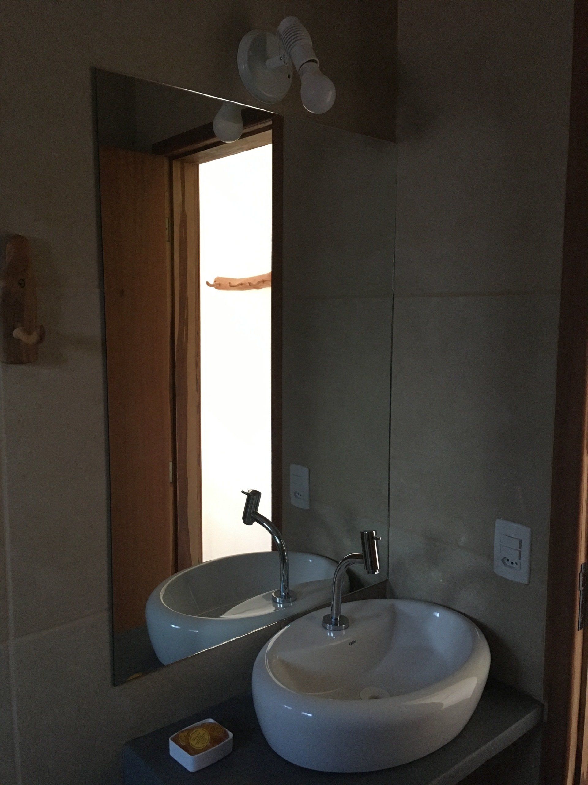 Banheiro com pia oval, espelho grande e luzes suspensas.