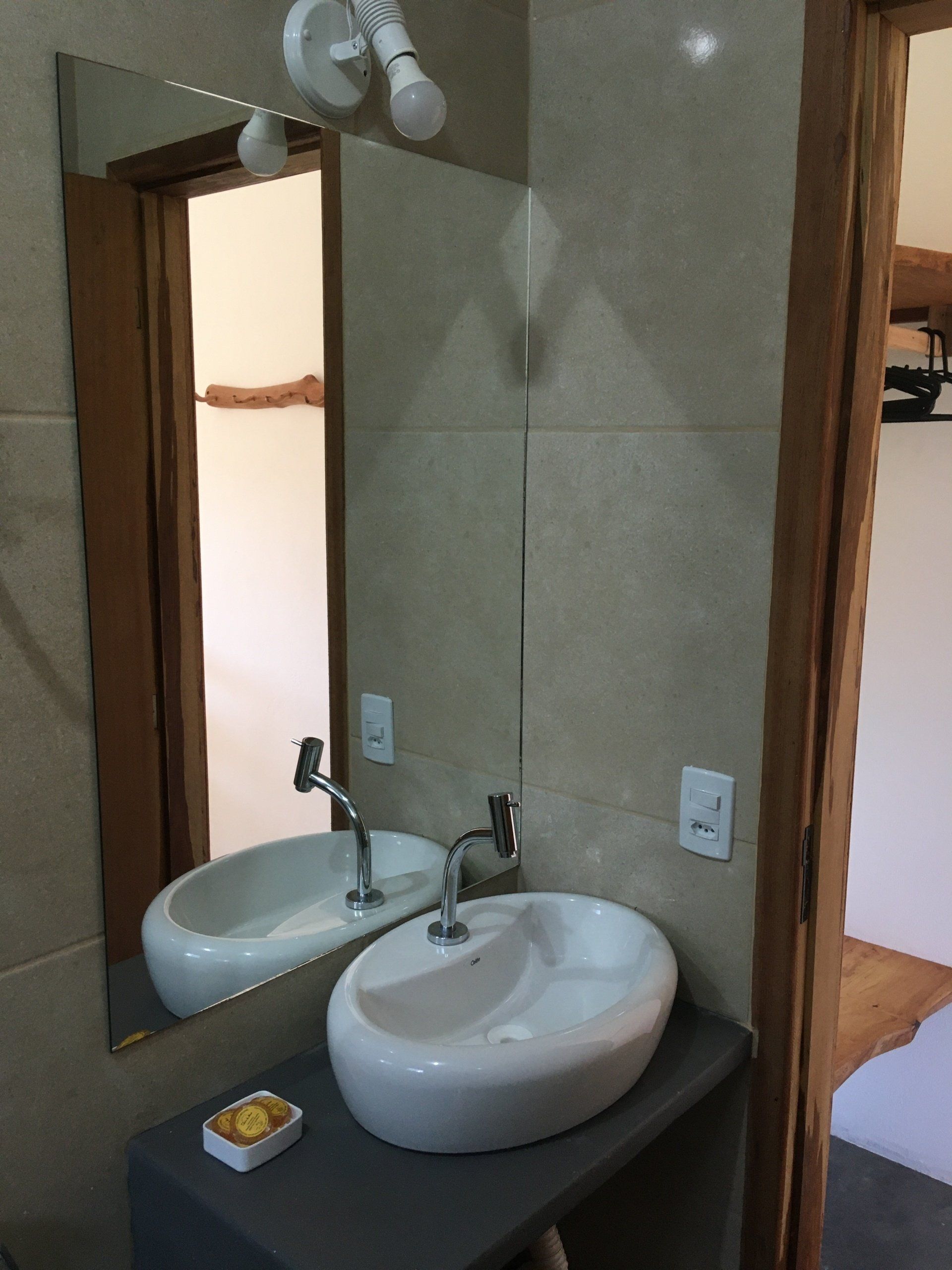 Pia de banheiro com cuba oval branca, espelho e azulejo neutro.