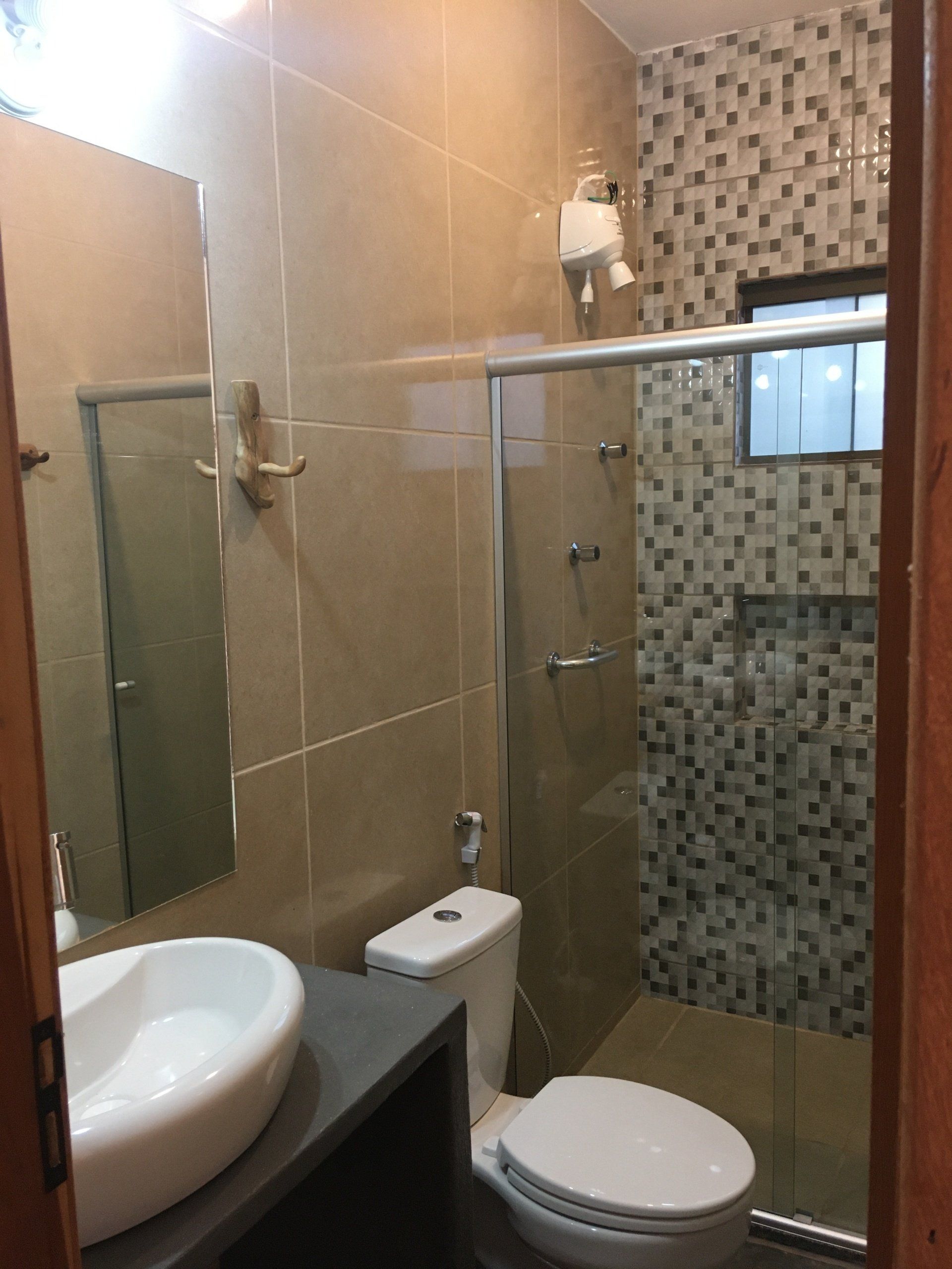 Banheiro com azulejo bege, vaso sanitário, chuveiro e pia brancos.