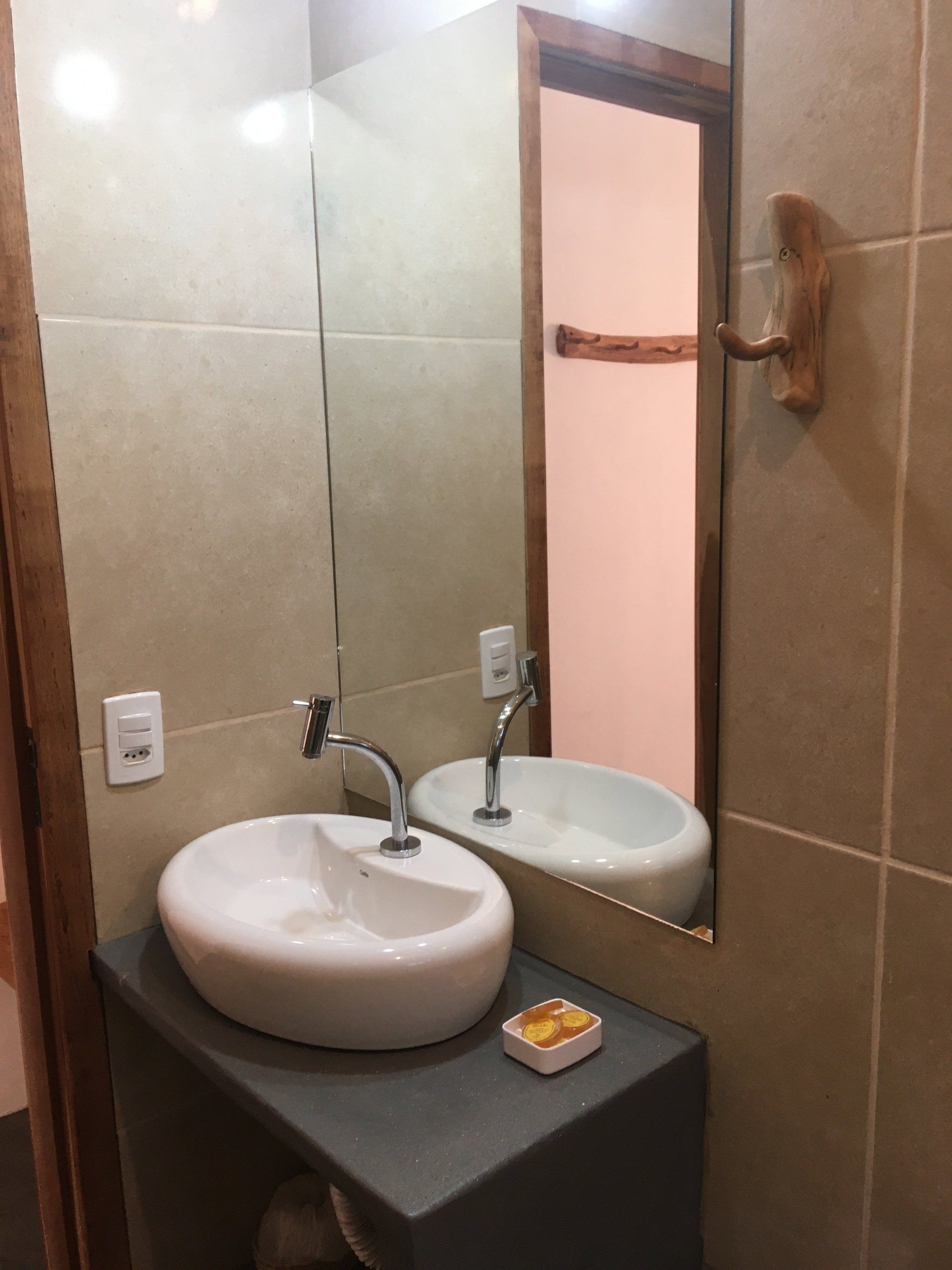 Pia de banheiro com cuba oval, bancada cinza, espelho e azulejo bege claro.