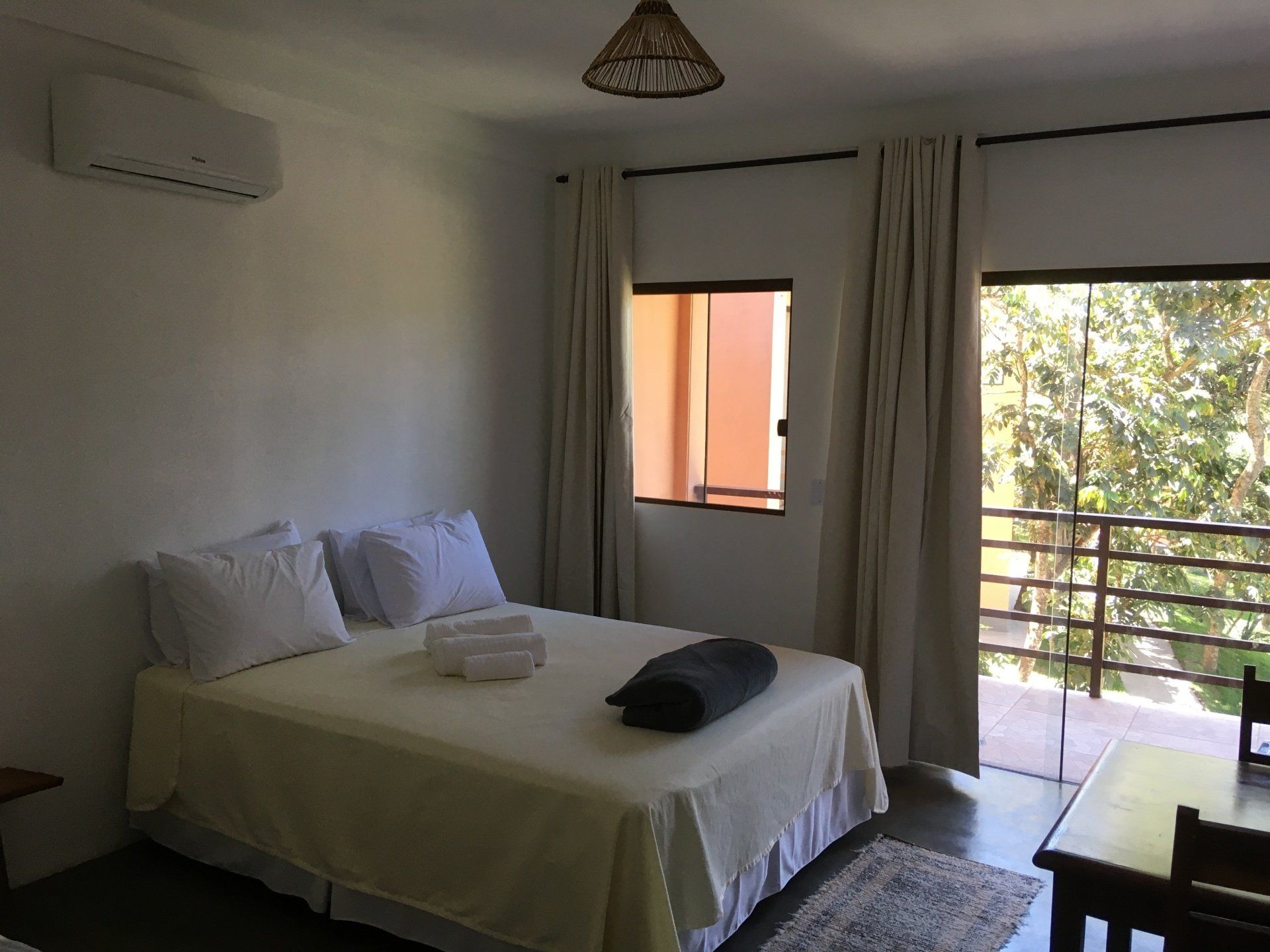 Quarto com cama, toalhas e varanda com vista para a área verde.
