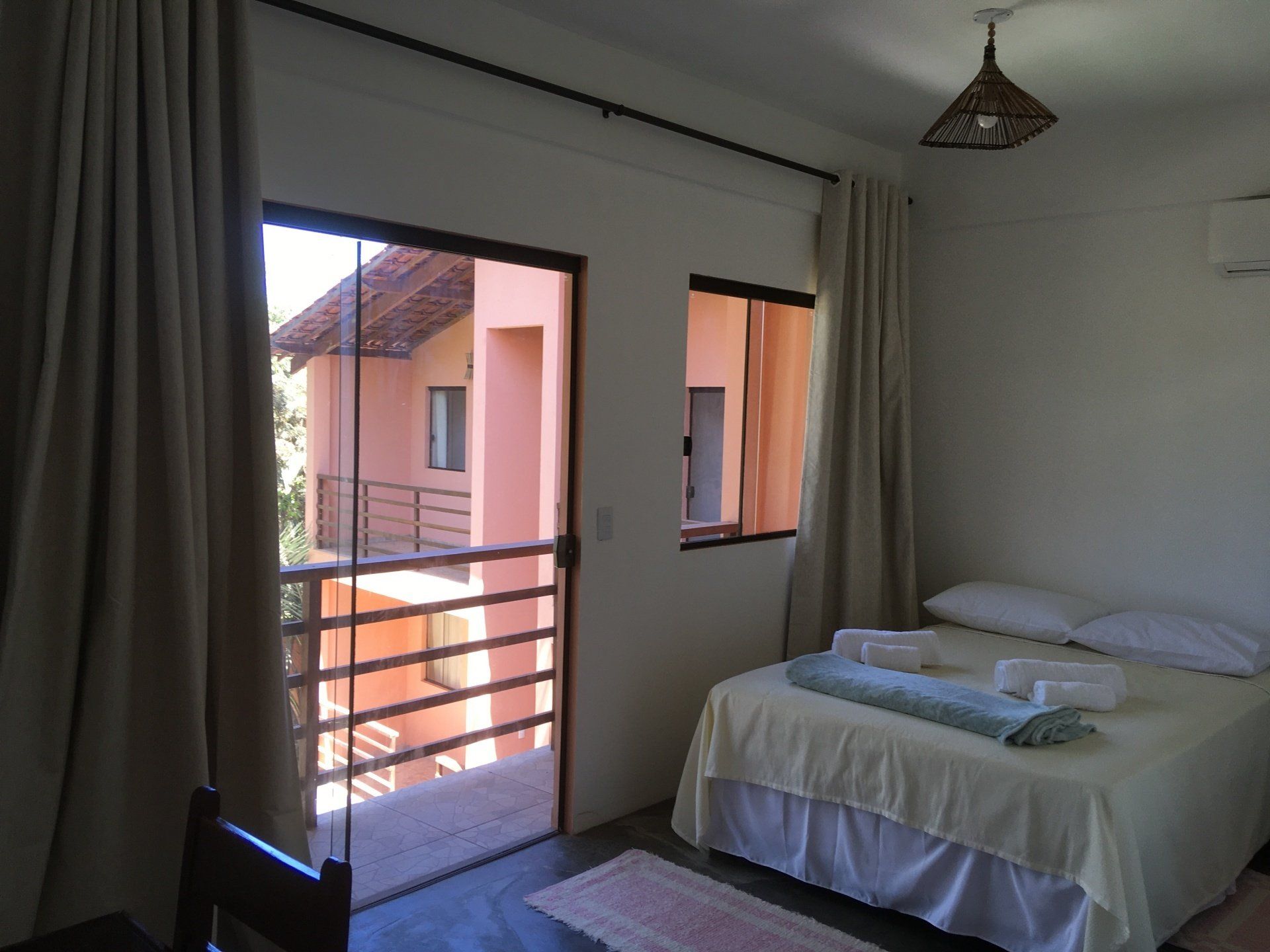 Quarto com cama, varanda e vista para um prédio cor de pêssego.