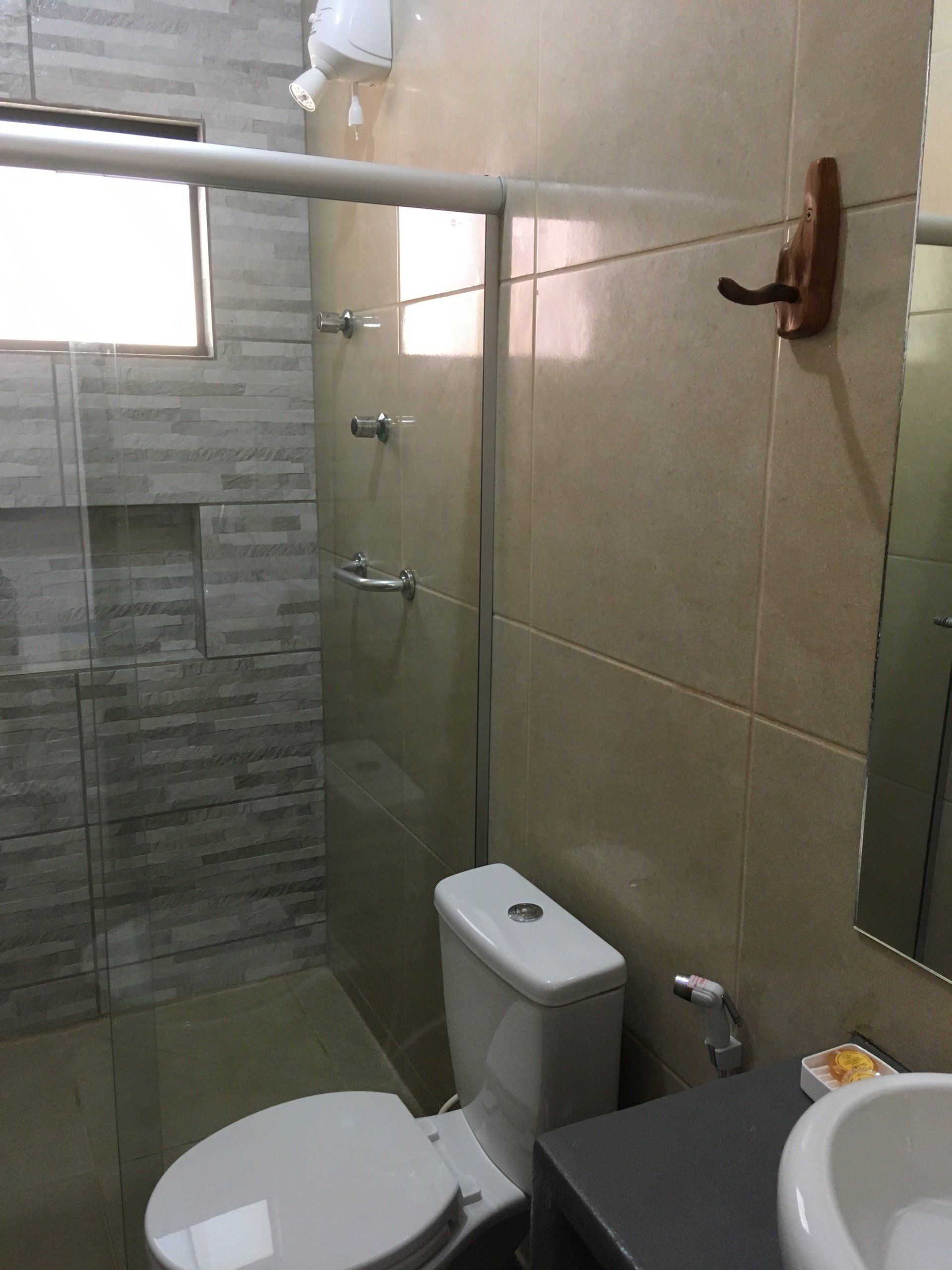 Banheiro com vaso sanitário branco, azulejos cinza no box e azulejos bege claro na parede.