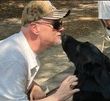 A man is kissing a black dog on the nose.