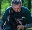 A man is holding a black dog in his arms.