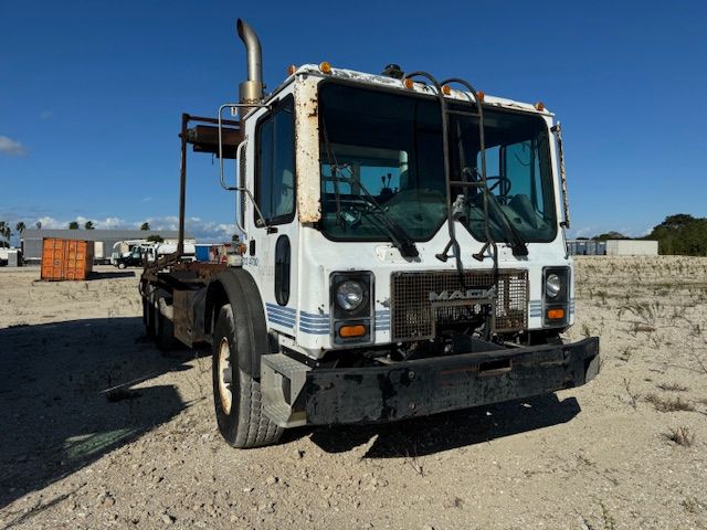 A white garbage truck is parked in a dirt field.