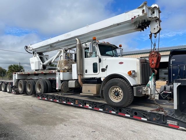 A white truck with a crane on top of it is on a trailer.