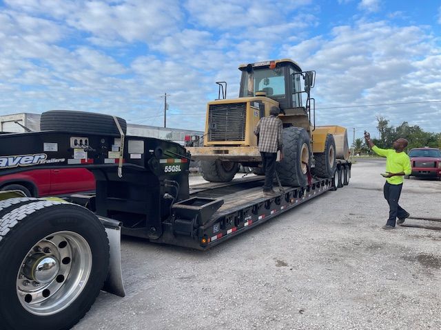 A man is standing next to a trailer with a tractor on it.