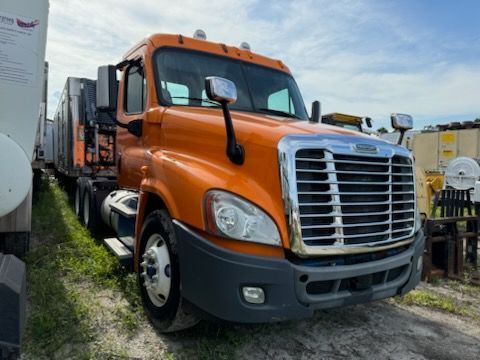 An orange semi truck is parked in a grassy field.