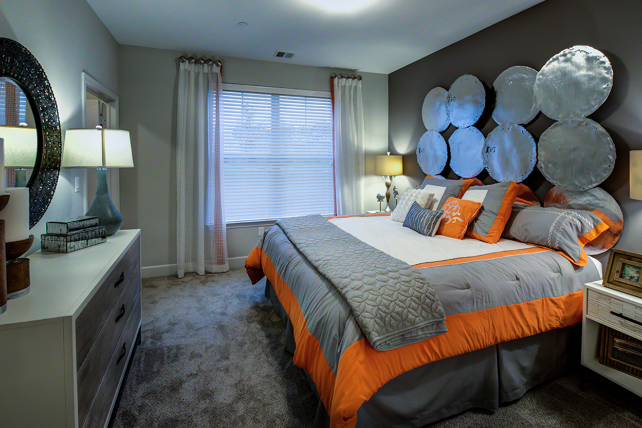 A bedroom with a large bed , dresser , nightstand and mirror.