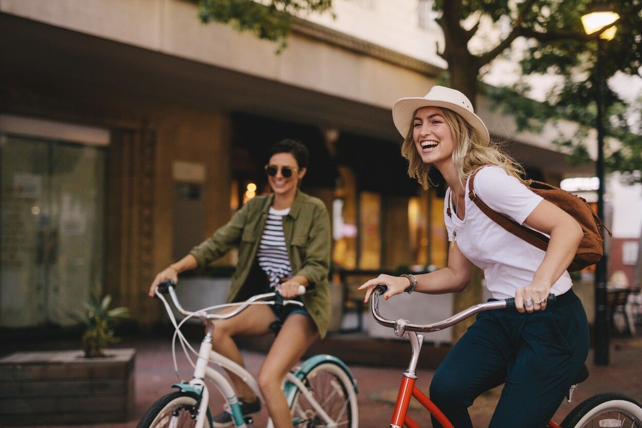 Two women are riding bicycles down a city street.