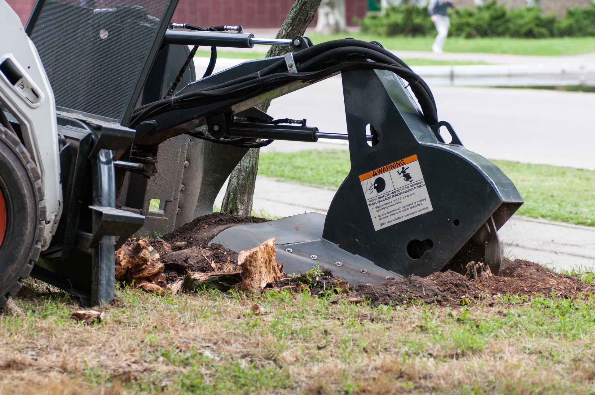 Excavator bucket removing a tree stump from a grassy roadside area