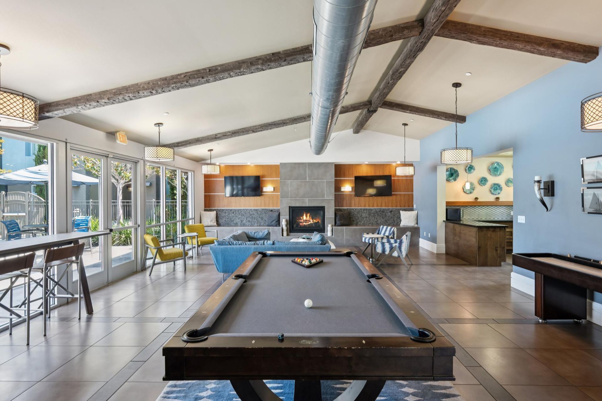 A game room with a pool table, shuffleboard, fireplace, seating, and outdoor access.