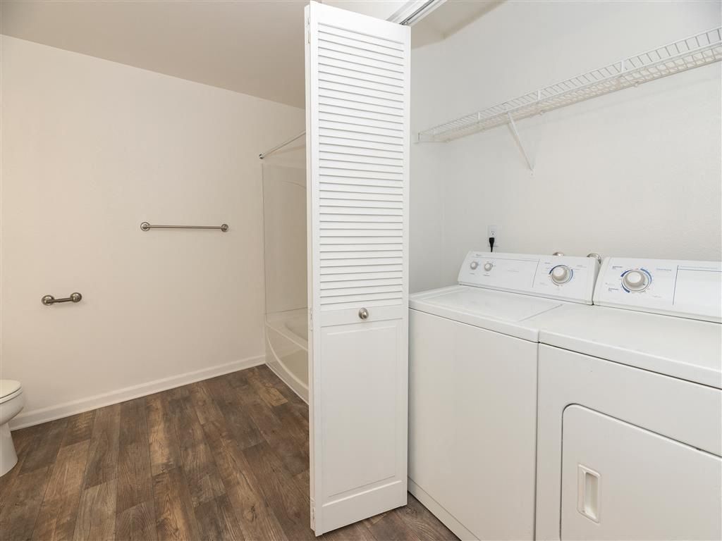 In-unit laundry area with a washer and dryer, white cabinet, and wood-look flooring.