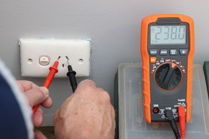 A person is using a multimeter to test an electrical outlet.