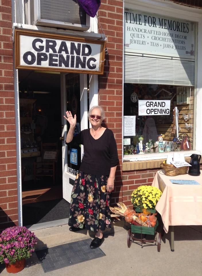 A owner is standing in front of a store with a sign that says grand opening