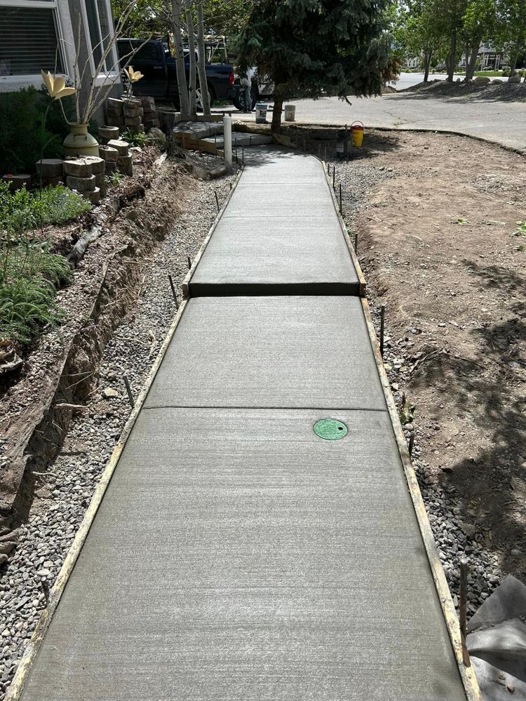 Newly poured concrete sidewalk with metal edging, surrounded by dirt and gravel.