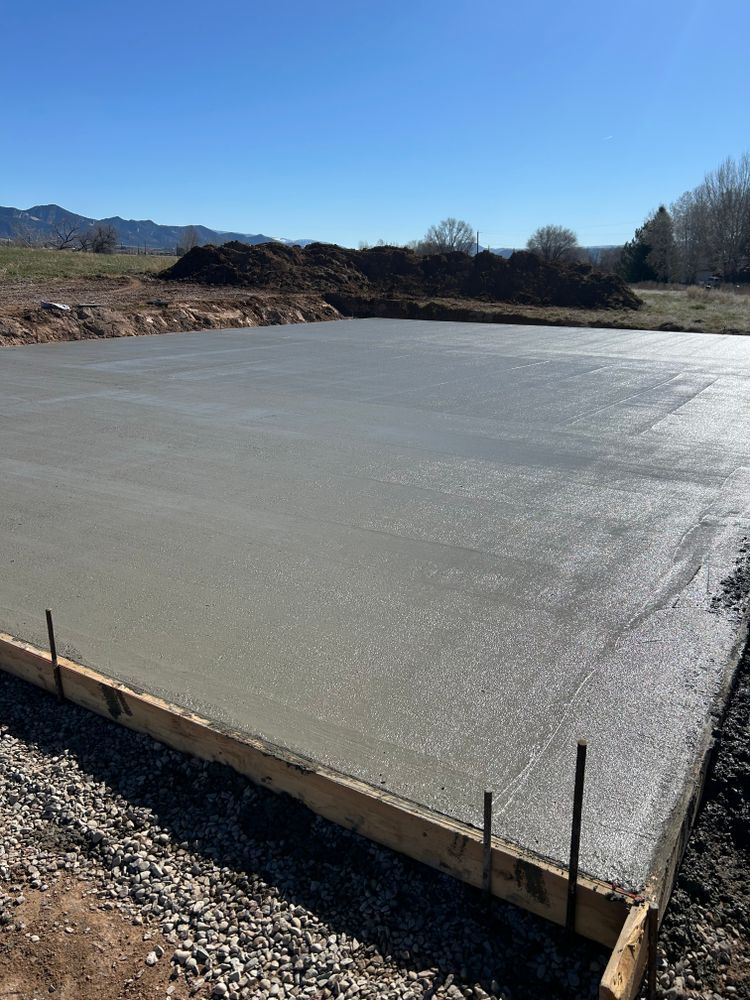 Freshly poured concrete slab in a wooden frame; outdoor setting with dirt and distant mountains.