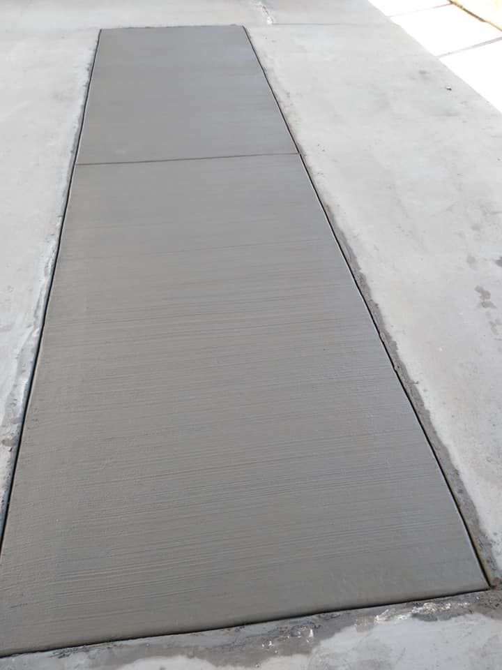 Freshly poured concrete rectangular slab, bordered by dark lines, set into a larger concrete surface.