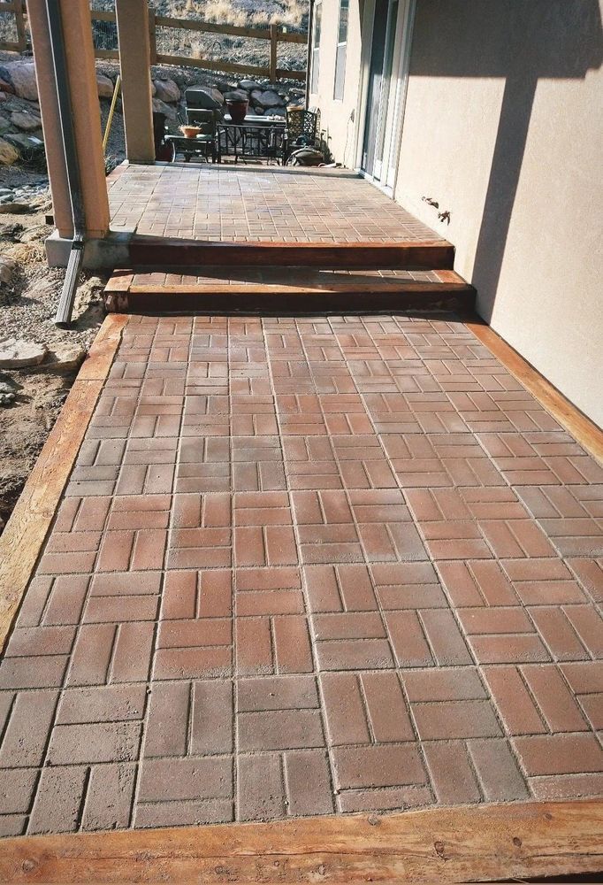 Brick patio with wooden borders leading to steps and a building entrance.