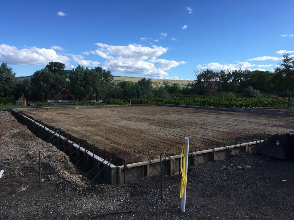 A prepared concrete foundation on a gravel base, with a blue sky and trees in the background.