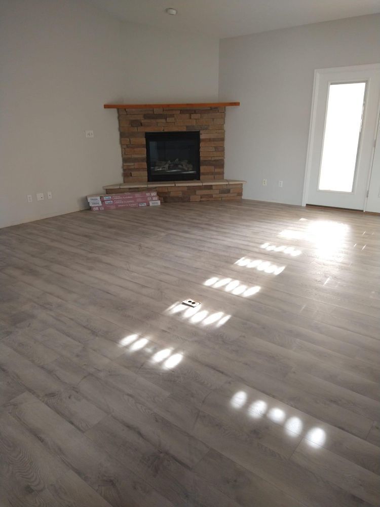 Empty room with light wood-look flooring, stone fireplace, and French door.